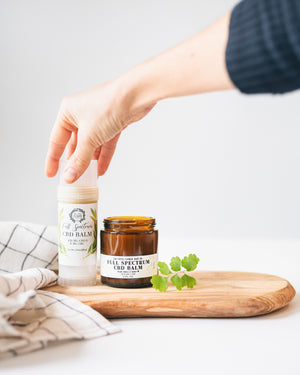 Full Spectrum CBD Balm 2.5 oz twist up tube and oz amber glass jar with hand reaching in to grab 